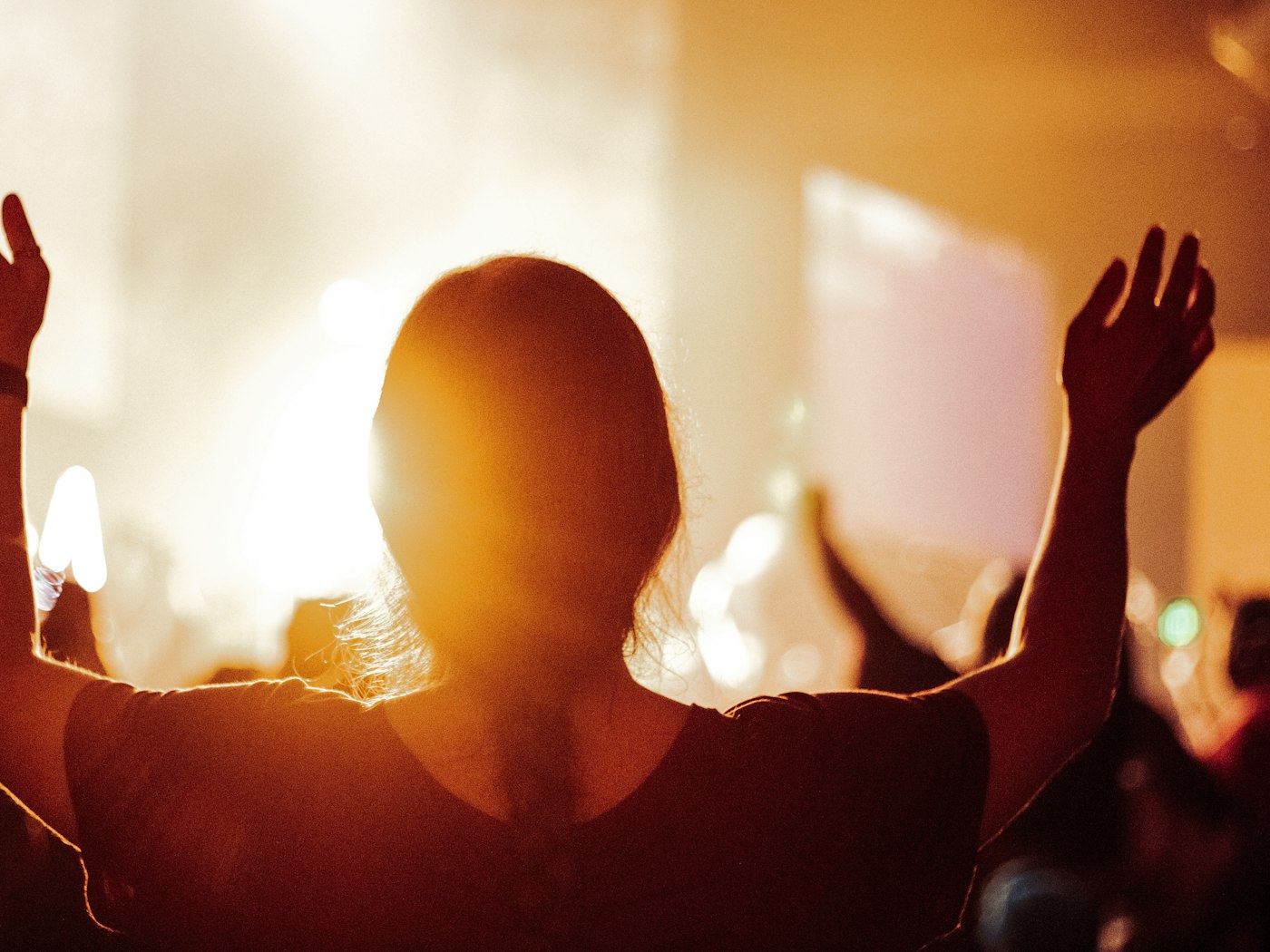 A woman with her arms raised, silhouetted against warm light