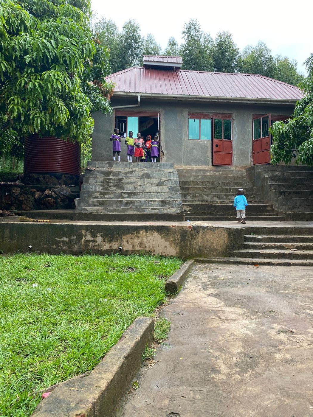 A church and school building with a red corrugated roof and red doors, with young children standing at the top of the concrete steps