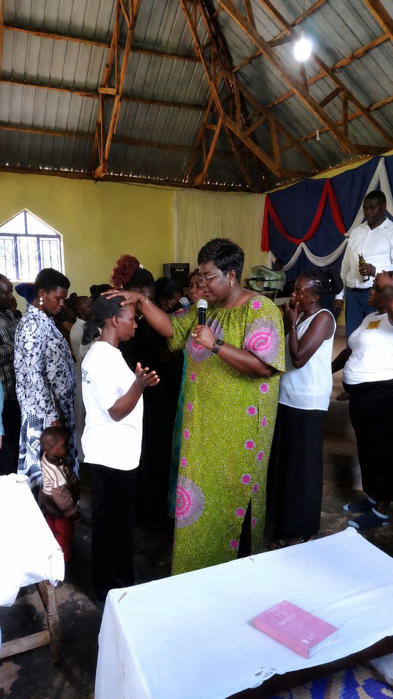 Rev. Josephine Harrison laying hands in prayer on a woman during a mission service, with the congregation gathered around